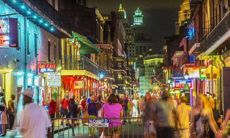 Vibrant Bourbon Street nightlife in New Orleans French Quarter, crowded pedestrians, neon signs, wrought-iron balconies and historic buildings at night