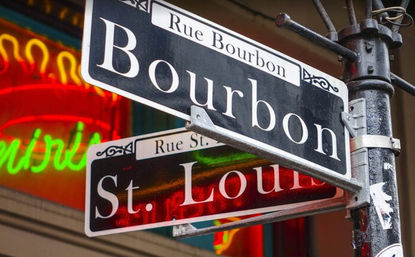 Close-up of black "Bourbon" and "St. Louis" street signs on a metal pole with colorful neon lights blurred in the background in New Orleans' French Quarter.
