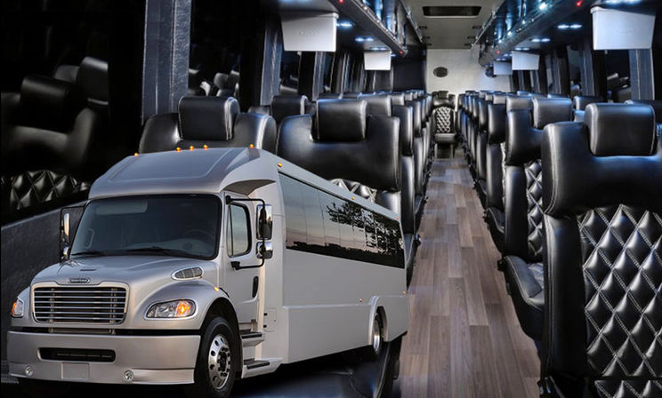 Luxury charter coach interior with quilted black leather captain seats, wood-look aisle flooring, ambient overhead lighting, and a white shuttle-style bus exterior in the foreground.