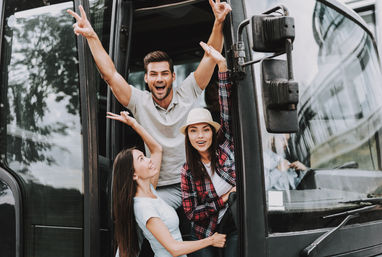 Three cheerful friends waving from the open door of a tour bus on an urban group trip
