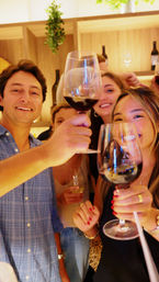 Friends clinking red wine glasses in a cozy wine bar, smiling and toasting during a lively night out.