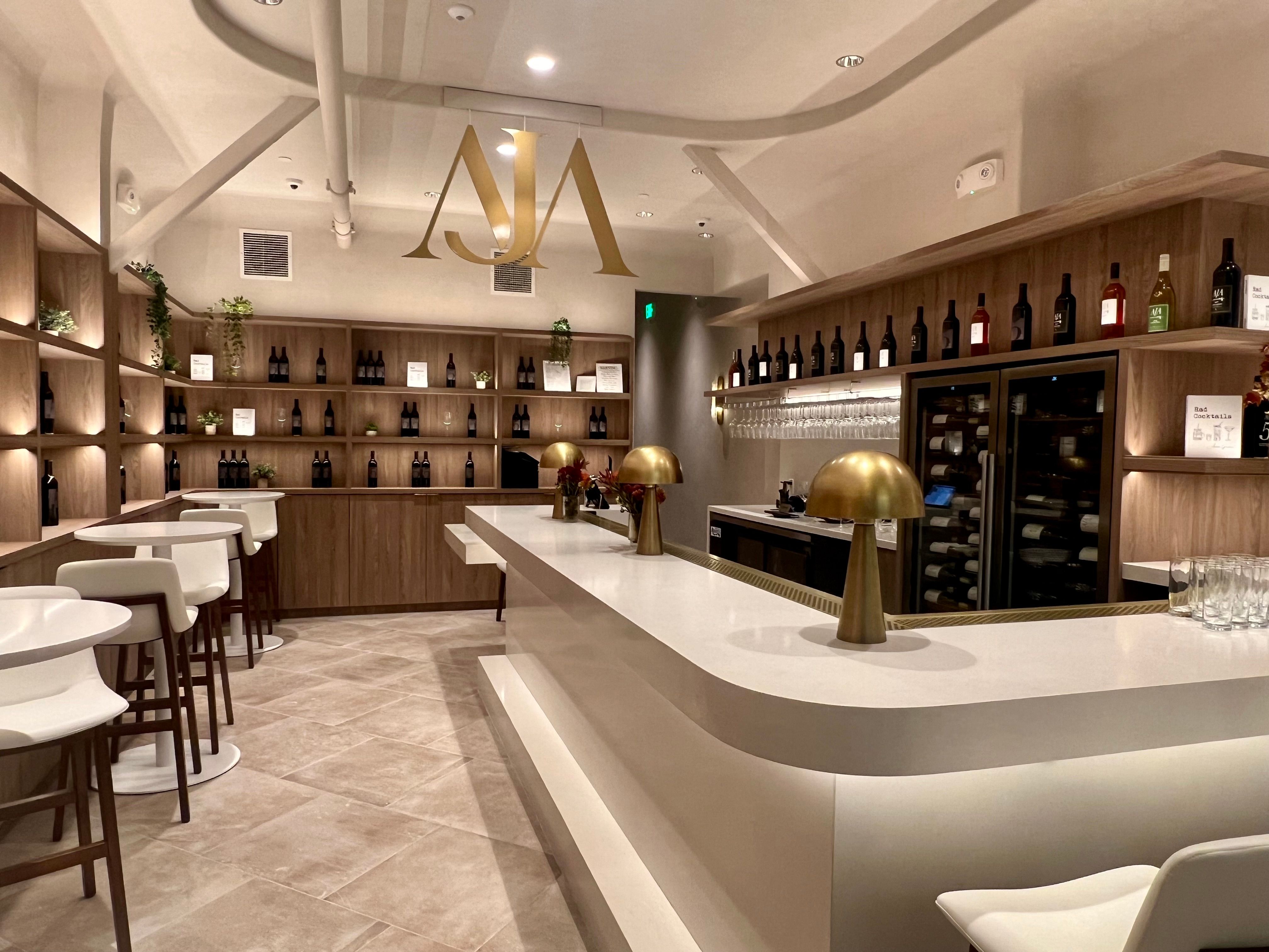 Inviting modern wine bar interior with curved white bar, brass mushroom lamps, white barstools, and wooden shelves lined with wine bottles and warm lighting.