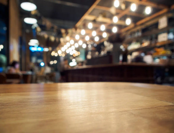 Empty wooden table in a cozy urban cafe with warm string lights and a blurred bar counter creating a bokeh background
