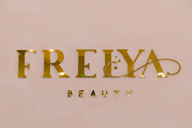Chic gold metallic beauty brand lettering in serif and script styles mounted on a blush-pink wall