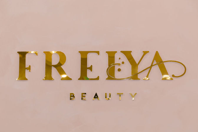 Chic gold metallic beauty brand lettering in serif and script styles mounted on a blush-pink wall
