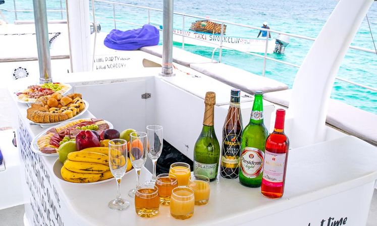 Catamaran deck brunch buffet with fresh fruit, pastries, champagne and cocktails on a white bar overlooking turquoise tropical sea.