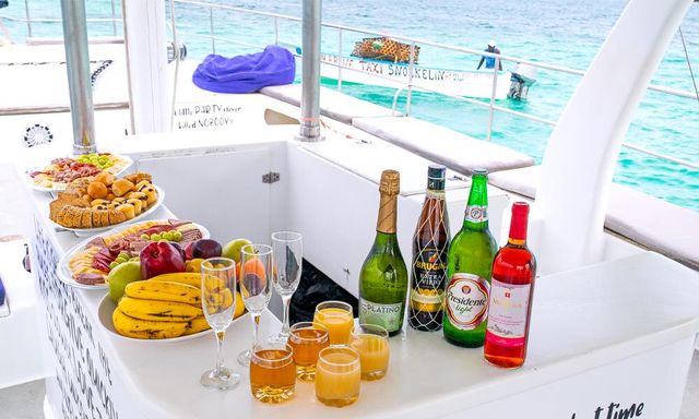 Catamaran deck brunch buffet with fresh fruit, pastries, champagne and cocktails on a white bar overlooking turquoise tropical sea.