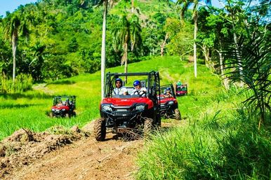 Group of red off-road UTVs on a dirt trail through lush tropical hills and palm trees, riders in helmets enjoying an outdoor adventure