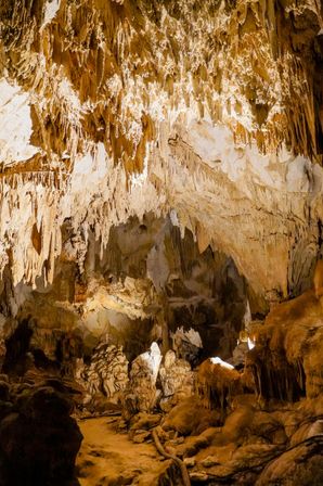 Limestone cave interior: hanging stalactites and rising stalagmites in a lit underground chamber with textured rock formations and a winding path