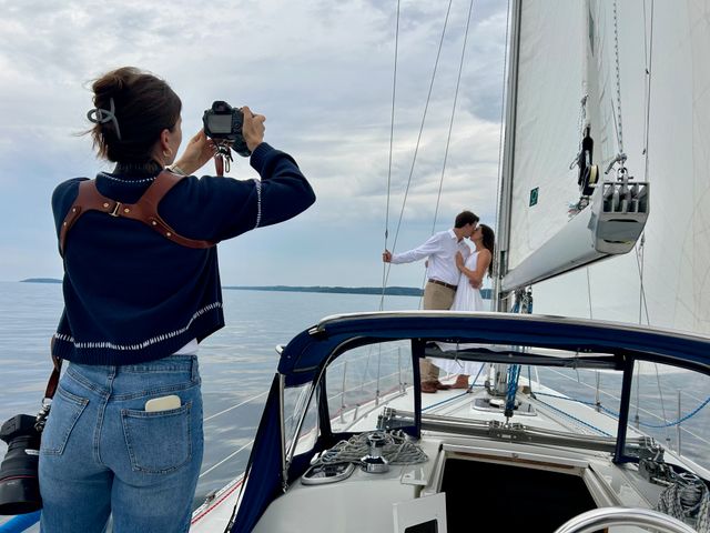 Photographer on a sailboat photographing a kissing couple by the mast with calm coastal waters and a cloudy sky backdrop