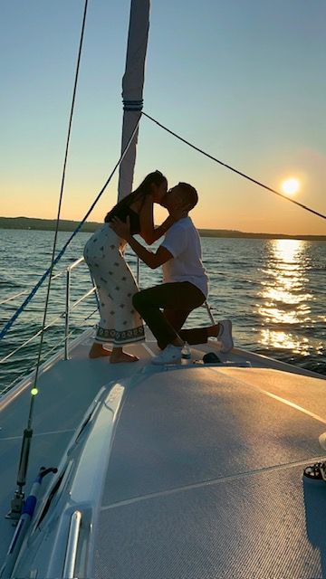 Couple kissing on the bow of a sailboat at golden sunset, sun glinting on calm ocean water