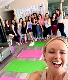 Smiling group selfie at a home yoga class with women in activewear striking celebratory poses on bright green and pink mats on a hardwood floor