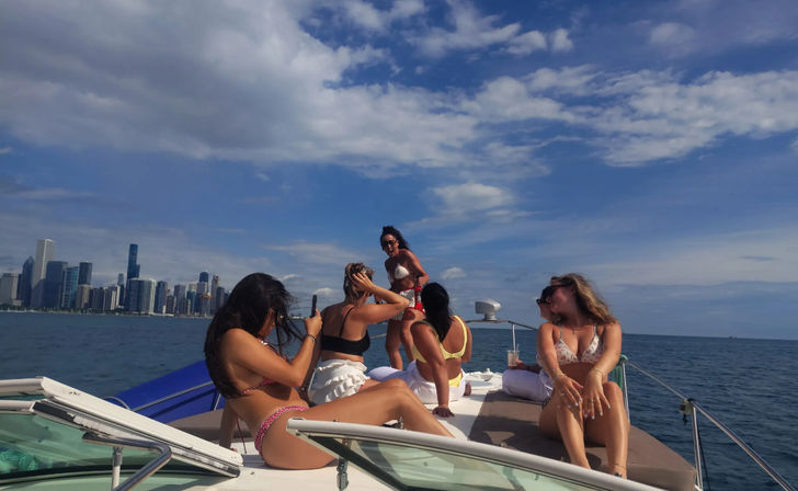 Group of women in bikinis enjoying a sunny boat party on Lake Michigan with the Chicago skyline and blue sky in the background