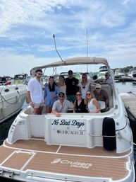 Group of friends smiling on the swim platform of a white motor yacht docked at a Chicago marina, transom reading 'No Bad Days, Chicago, IL' under a partly cloudy summer sky.