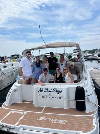 Group of friends smiling on the swim platform of a white motor yacht docked at a Chicago marina, transom reading 'No Bad Days, Chicago, IL' under a partly cloudy summer sky.