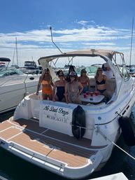 Group of friends in swimsuits enjoying a summer boat party on a white motor yacht in a busy Chicago, IL marina under a bright blue sky