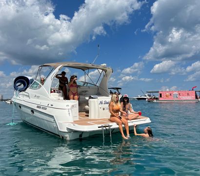 Friends lounging on a white motorboat in turquoise water under a bright blue sky with puffy clouds, summer boating scene