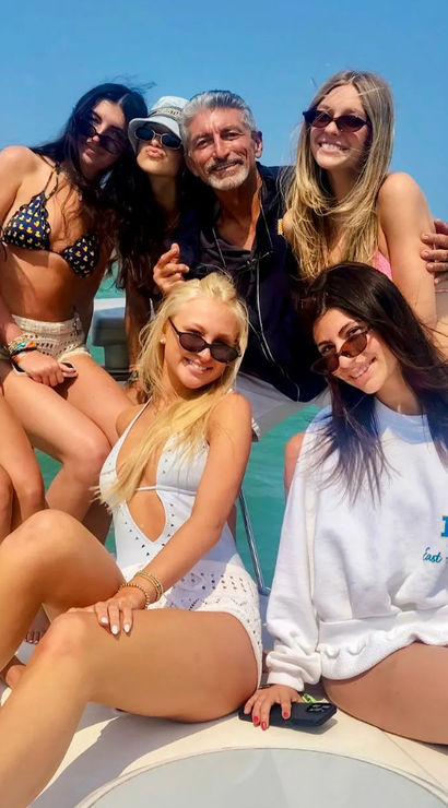 Group of seven adults posing on a boat cruise in bikinis and sunglasses, smiling on a sunny summer day over turquoise tropical ocean water.
