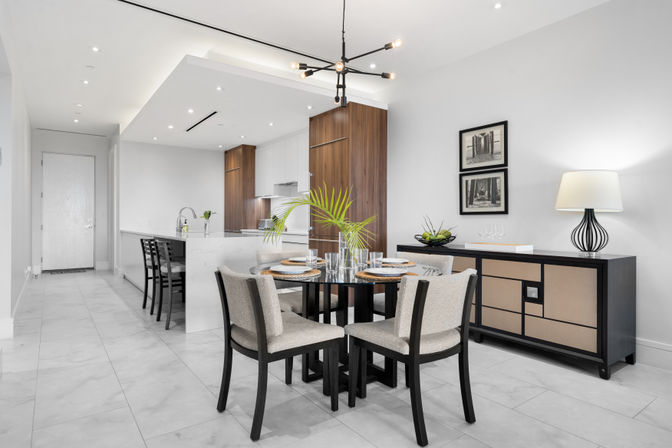 Modern open-concept dining and kitchen in an urban condo — round glass table with four upholstered chairs, marble tile floor, walnut cabinets, breakfast island with bar stools, black sideboard and sputnik chandelier