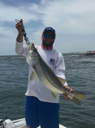 Proud angler holding a large saltwater snook with a lip gripper on a boat over choppy coastal waters under a cloudy sky