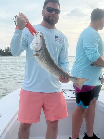 Angler holding a large redfish on a fishing boat inshore near Anna Maria Island, Florida at sunset — coastal saltwater fishing