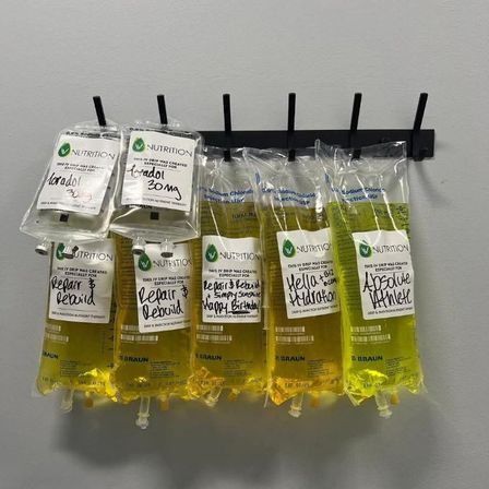 Row of bright yellow vitamin IV drip bags hanging on wall hooks in a wellness clinic, each labeled for customized hydration and nutrient treatments.