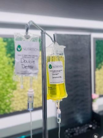 Bright yellow "Inner Immune" IV drip and a clear "Double Detox" bag hanging from a stainless pole in a modern wellness clinic IV therapy room.