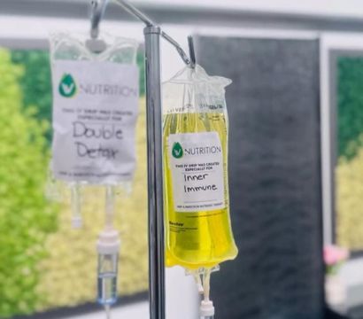 Bright yellow "Inner Immune" IV drip and a clear "Double Detox" bag hanging from a stainless pole in a modern wellness clinic IV therapy room.