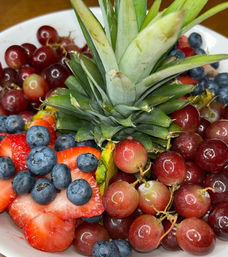 Close-up of a vibrant fruit bowl with a pineapple crown centerpiece surrounded by sliced strawberries, juicy blueberries and red grapes