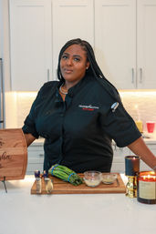 Chef in a black coat in a modern white kitchen preparing asparagus on a wooden cutting board with knives and small glass seasoning bowls.