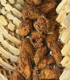 Close-up overhead of crispy golden fried chicken wings piled between cut waffles dusted with powdered sugar — classic chicken-and-waffles comfort food