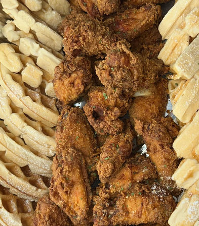 Close-up overhead of crispy golden fried chicken wings piled between cut waffles dusted with powdered sugar — classic chicken-and-waffles comfort food