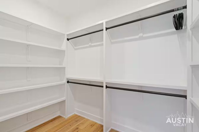 Bright, modern empty walk-in closet with white built-in shelves, black hanging rods, a few black hangers and hardwood flooring.