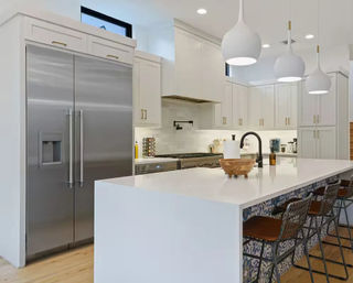 Bright modern white kitchen with a large waterfall island, stainless steel French-door refrigerator, three pendant lights, and patterned bar stools
