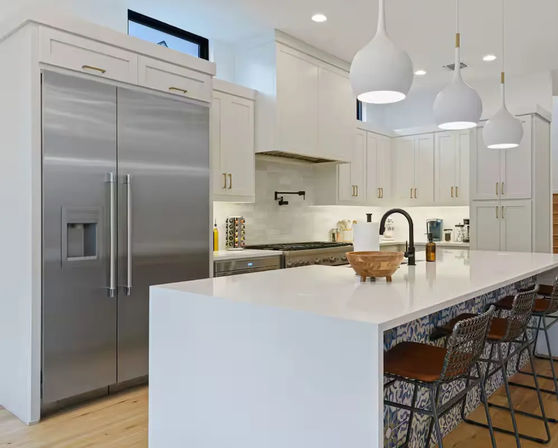 Bright modern white kitchen with a large waterfall island, stainless steel French-door refrigerator, three pendant lights, and patterned bar stools
