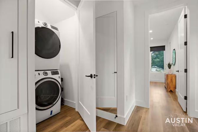 Light-filled Austin apartment hallway with stacked washer/dryer in a closet, crisp white doors and trim, warm hardwood floors, and a sunlit bedroom at the end of the hall.