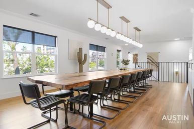 Bright Austin loft dining area with a long live-edge wood table flanked by black cantilever chairs, globe pendant lights, large windows with tree views, hardwood floors and modern decor.