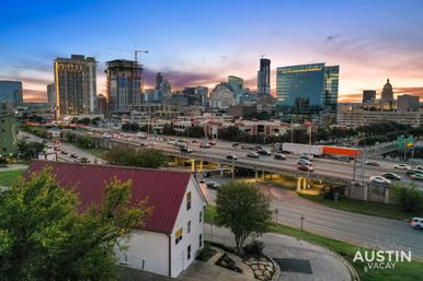 Austin, Texas skyline at dusk with glass skyscrapers and a construction crane, rush-hour traffic on an elevated highway and a red-roof house in the foreground.
