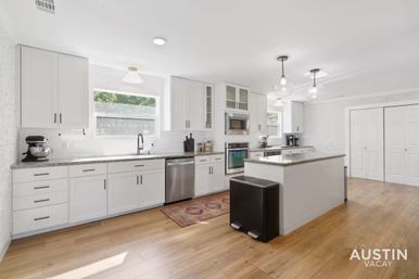 Bright modern white kitchen in Austin, Texas with island, stainless steel appliances, hardwood floors and pendant lights.