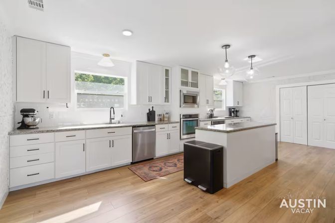 Bright modern white kitchen in Austin, Texas with island, stainless steel appliances, hardwood floors and pendant lights.