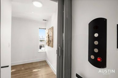 Mini modern elevator landing with folding door, wood floors, white walls, three-button control panel and a small window framing a distant city skyline