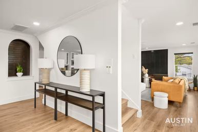 Bright modern Austin home entryway opening to a living room, featuring a black metal console with round mirror and lamps, light wood floors, an arched plant niche, and a mustard sofa.