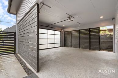 Sleek modern two-car residential garage with frosted glass sectional door, speckled epoxy floor, dark horizontal wood-slat privacy walls and ceiling-mounted opener.