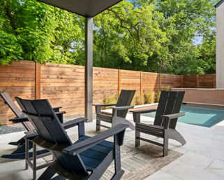 Modern covered backyard patio with dark Adirondack chairs, small rectangular pool, wooden privacy fence and lush green trees