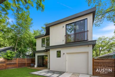 Sunny modern two-story Austin home with angled roof, second-floor balcony, single-car garage, fenced yard and small patio amid leafy trees