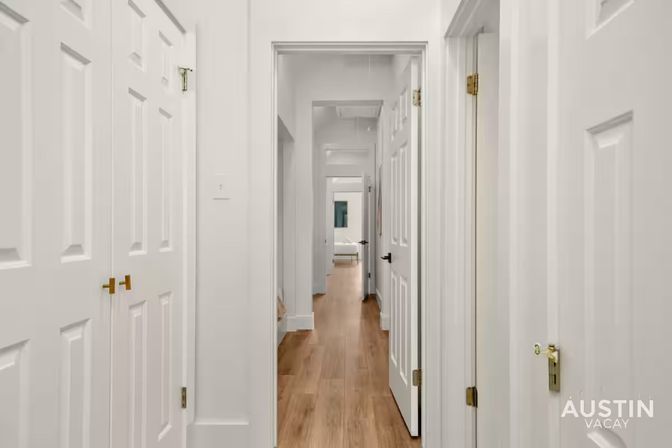Bright modern home hallway with warm wood flooring, lined with white paneled doors and a glimpse of a bedroom at the end.