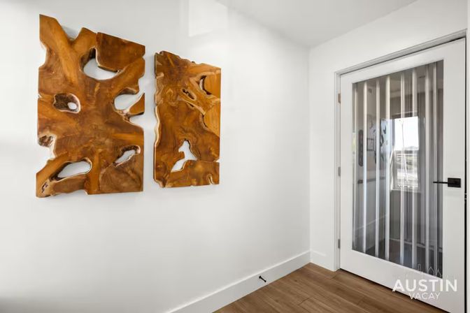 Bright modern hallway with white walls and wood floors, featuring two live-edge carved wood wall panels and a glass-paneled door with vertical blinds.