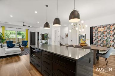 Bright modern open-plan kitchen and living room with large island, black pendant lights, blue accent chairs, yellow curtains and a floral-accent dining wall