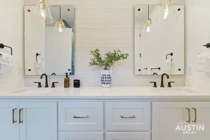 Bright spa-like double-sink bathroom vanity with white countertop, matte-black faucets, twin mirrors, glass pendant lights and a vase of greenery — Austin, TX