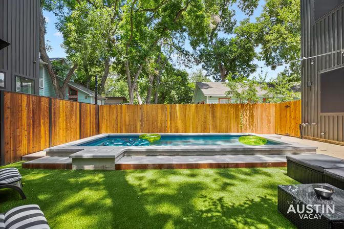 Sunny Austin backyard with a modern rectangular plunge pool, wooden privacy fence, artificial turf, striped lounge chairs and green inflatable pool floats
